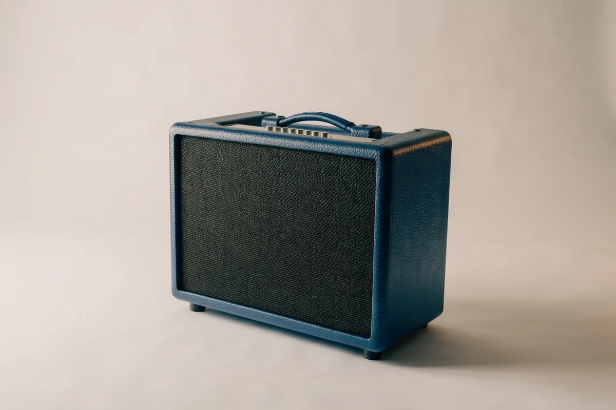 A deep cobalt-blue unbranded combo guitar amplifier with a charcoal speaker grille, top controls, and carry handle sits alone on a plain neutral surface, illustrating the best guitar amps for live performance.